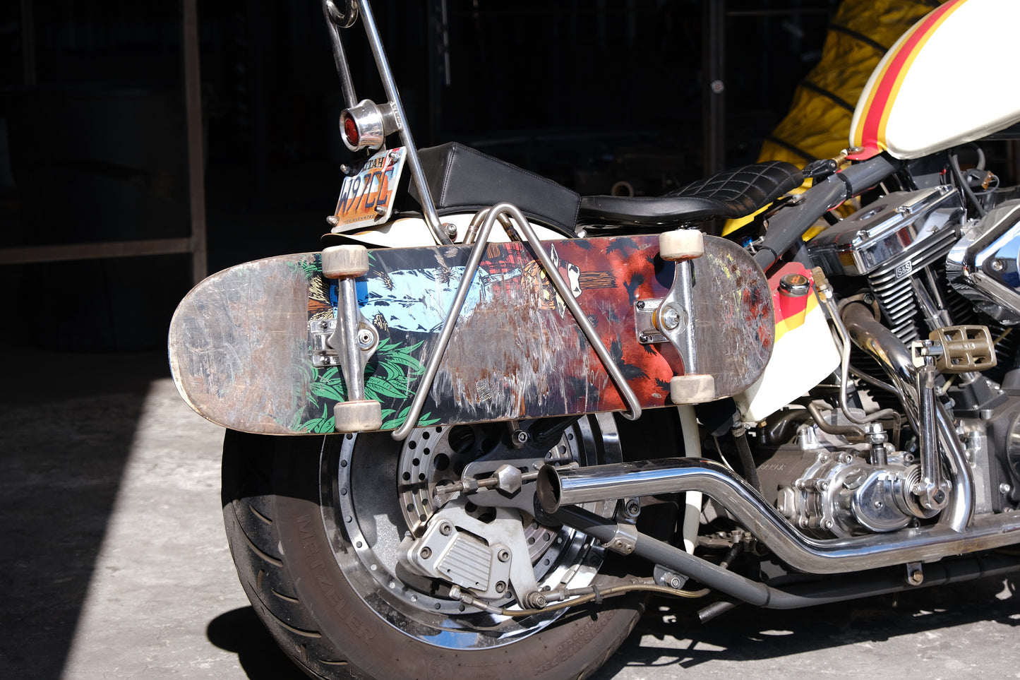 Edward Richie Motorcycle Skateboard rack in stainless steel with a skateboard in it mounted on a custom harley back side view